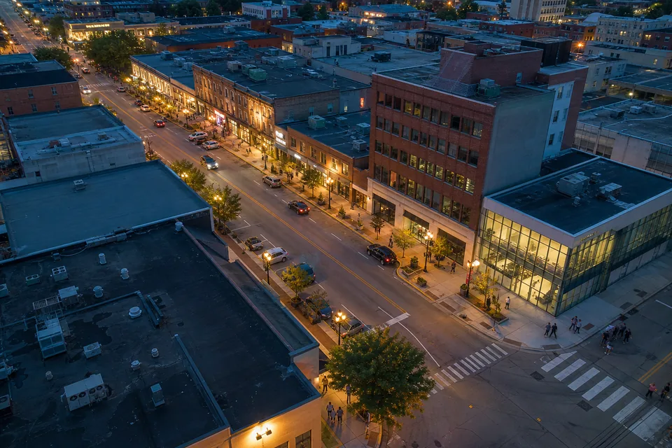 Aerial view of a mid-sized American downtown at dusk with lit streets, storefronts, a clinic and offices along a main avenue